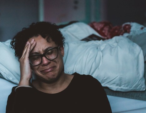 woman crying next to her bed.